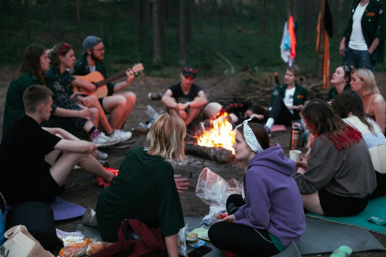 A diverse group of friends enjoying a campfire gathering in the forest during the evening.