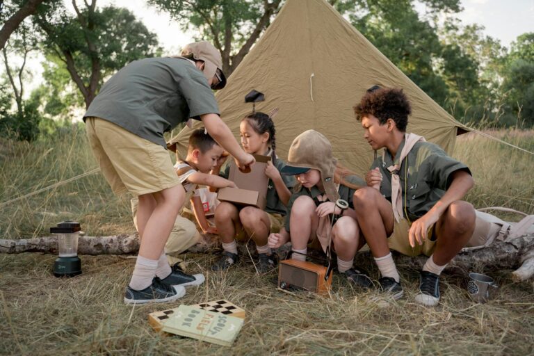 A group of young scouts gathers around a tent, exploring and bonding during a summer camping trip.